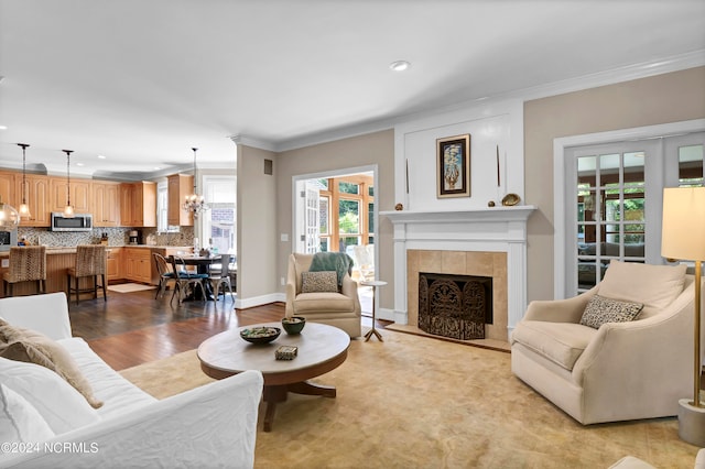 living room featuring a tiled fireplace, light wood-type flooring, crown molding, and an inviting chandelier