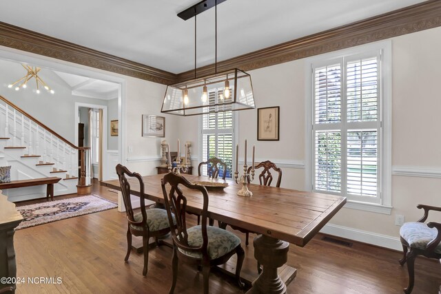 dining space with dark wood-type flooring, an inviting chandelier, and crown molding