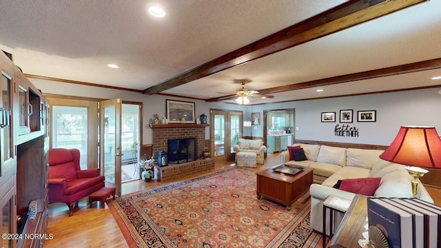 living room with light hardwood / wood-style floors, beamed ceiling, a textured ceiling, a fireplace, and french doors