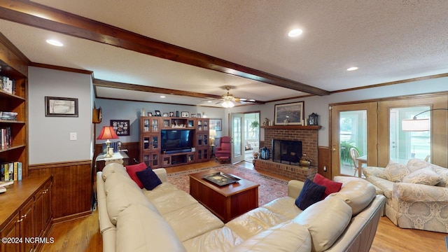 living room featuring ornamental molding, beam ceiling, a textured ceiling, a fireplace, and light wood-type flooring