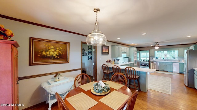 dining space featuring light hardwood / wood-style flooring, ceiling fan, sink, and crown molding