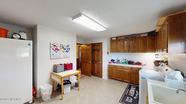 kitchen with sink, white refrigerator, independent washer and dryer, and a textured ceiling