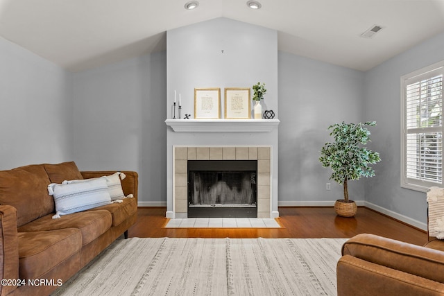 living area featuring wood finished floors, baseboards, visible vents, lofted ceiling, and a tiled fireplace