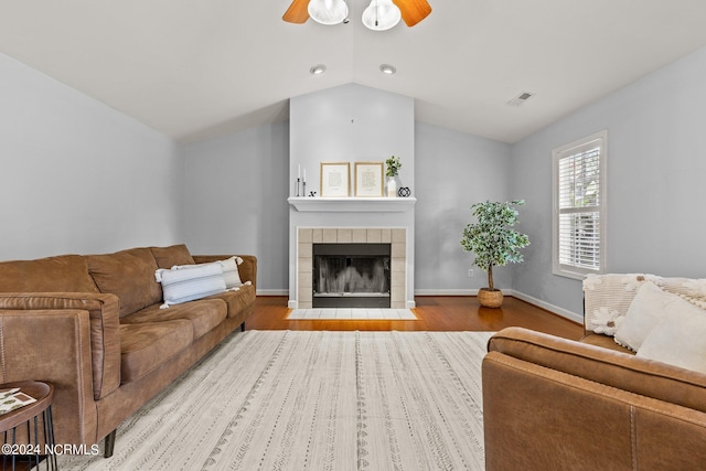 living area featuring wood finished floors, a ceiling fan, baseboards, a tile fireplace, and vaulted ceiling