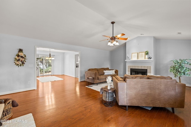 living area featuring a tiled fireplace, ceiling fan with notable chandelier, wood finished floors, baseboards, and vaulted ceiling