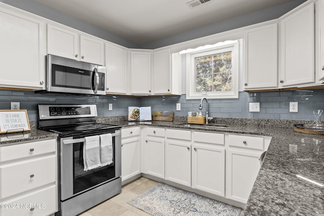 kitchen featuring dark stone countertops, a sink, decorative backsplash, appliances with stainless steel finishes, and white cabinetry