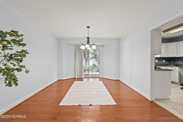 unfurnished dining area with an inviting chandelier, light wood-style floors, and baseboards