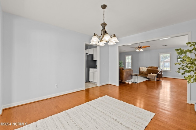 living area with ceiling fan with notable chandelier, baseboards, and light wood finished floors