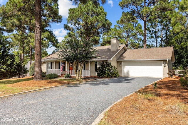 single story home with a porch, an attached garage, a chimney, and driveway