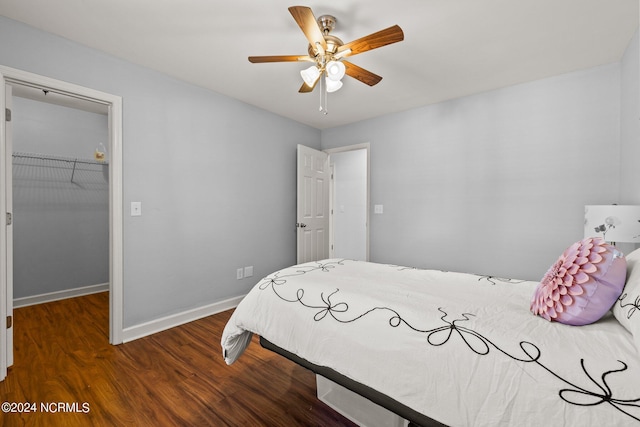 bedroom with a spacious closet, baseboards, wood finished floors, a closet, and a ceiling fan