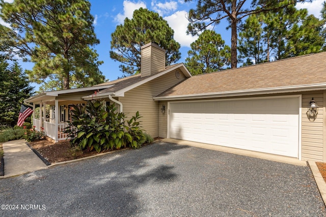 view of home's exterior featuring a shingled roof, a garage, driveway, and a chimney