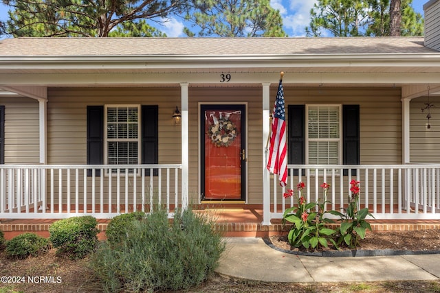 view of exterior entry featuring roof with shingles, covered porch, and a chimney