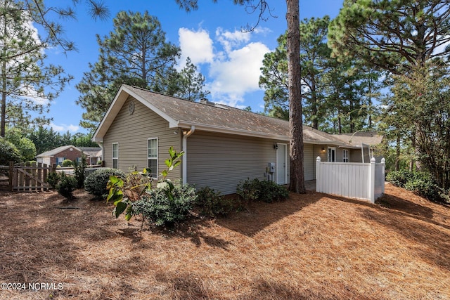 view of side of property with fence and a shingled roof