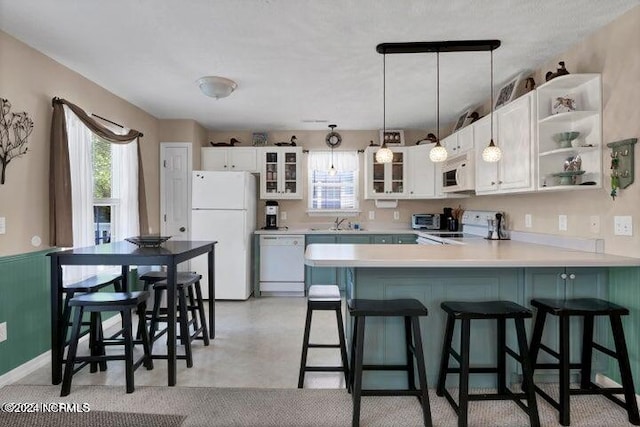 kitchen with a wealth of natural light, white appliances, decorative light fixtures, and white cabinets