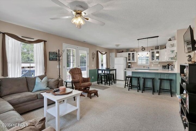 living room with ceiling fan, plenty of natural light, a textured ceiling, and light colored carpet