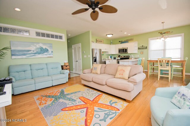 living room with ceiling fan with notable chandelier and light hardwood / wood-style flooring