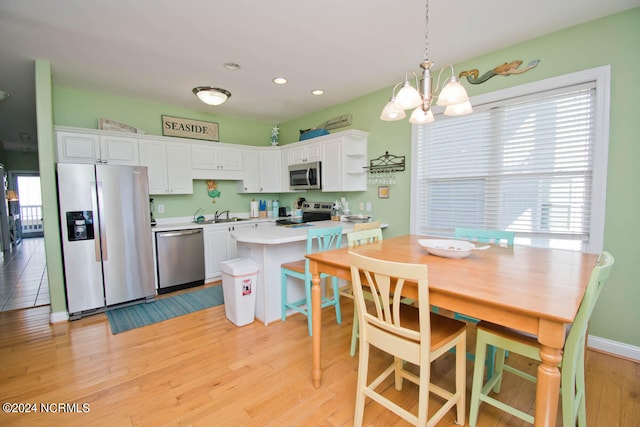 kitchen with light wood-type flooring, white cabinets, a notable chandelier, appliances with stainless steel finishes, and decorative light fixtures