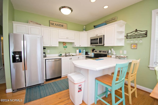 kitchen with light wood-type flooring, sink, white cabinets, appliances with stainless steel finishes, and a kitchen bar