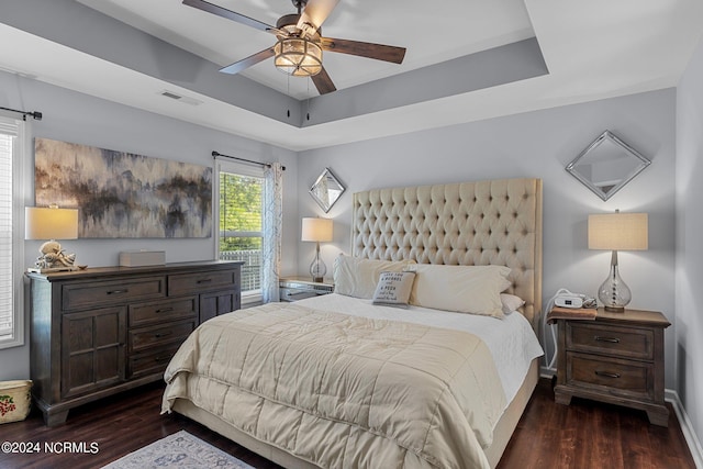 bedroom featuring dark hardwood / wood-style floors, ceiling fan, and a tray ceiling