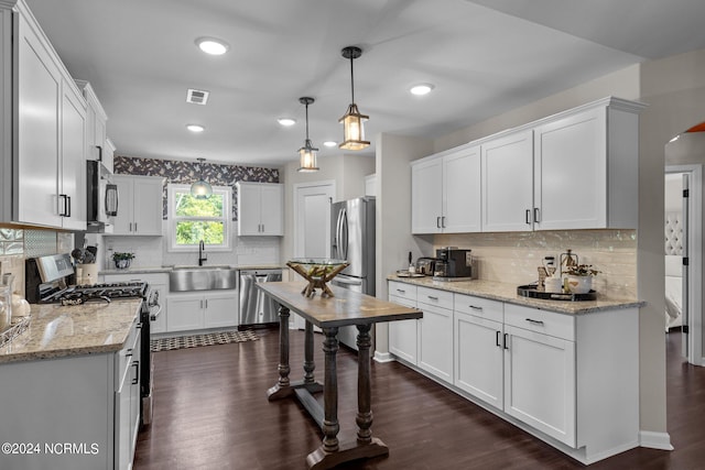 kitchen featuring appliances with stainless steel finishes, dark wood-type flooring, sink, pendant lighting, and white cabinets