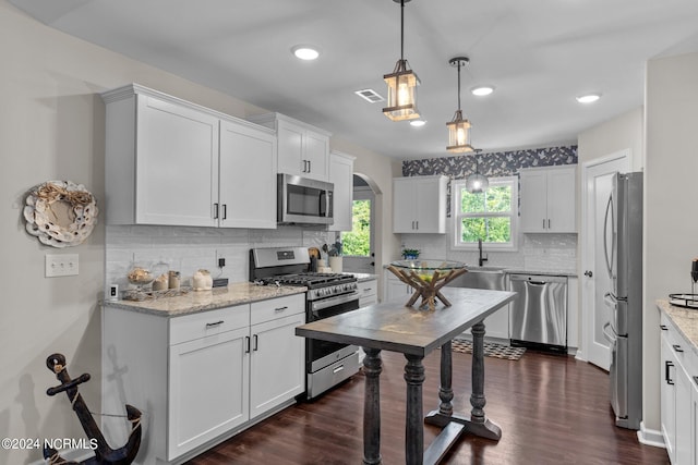 kitchen with light stone countertops, dark wood-type flooring, pendant lighting, white cabinets, and appliances with stainless steel finishes