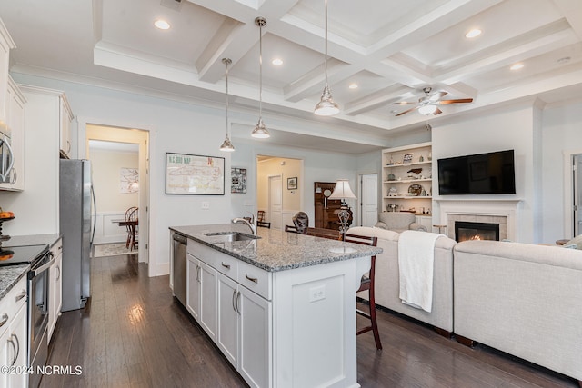 kitchen featuring an island with sink, white cabinetry, a tiled fireplace, hanging light fixtures, and stainless steel appliances