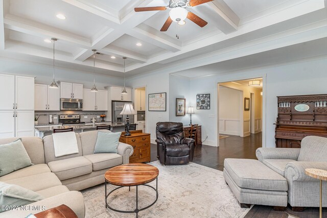 living room with ceiling fan, beamed ceiling, wood-type flooring, coffered ceiling, and crown molding