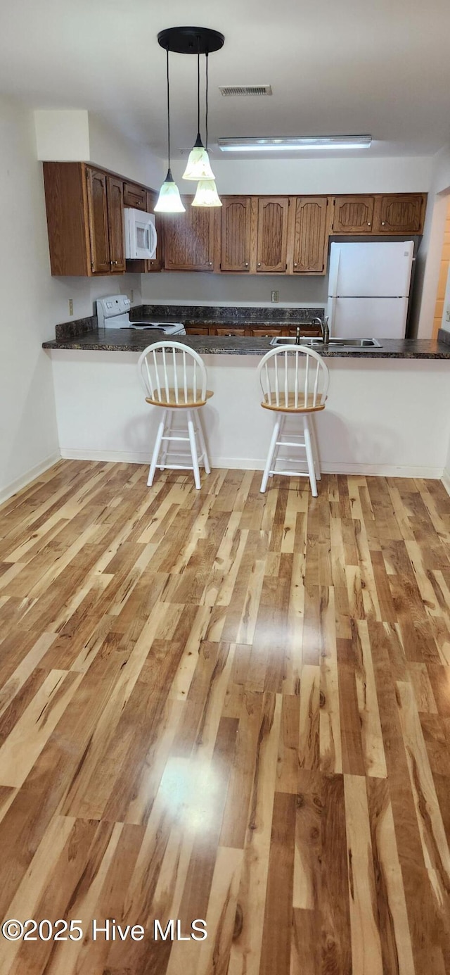 kitchen featuring white appliances, dark countertops, visible vents, and light wood-style floors