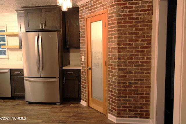 kitchen with dark hardwood / wood-style flooring, stainless steel appliances, dark brown cabinetry, crown molding, and brick wall