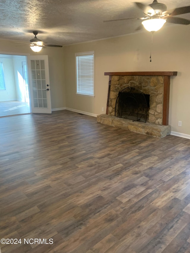 unfurnished living room with ceiling fan, a stone fireplace, a textured ceiling, and dark hardwood / wood-style flooring