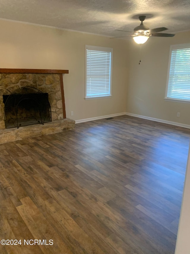 unfurnished living room featuring a textured ceiling, a stone fireplace, dark hardwood / wood-style flooring, and ceiling fan