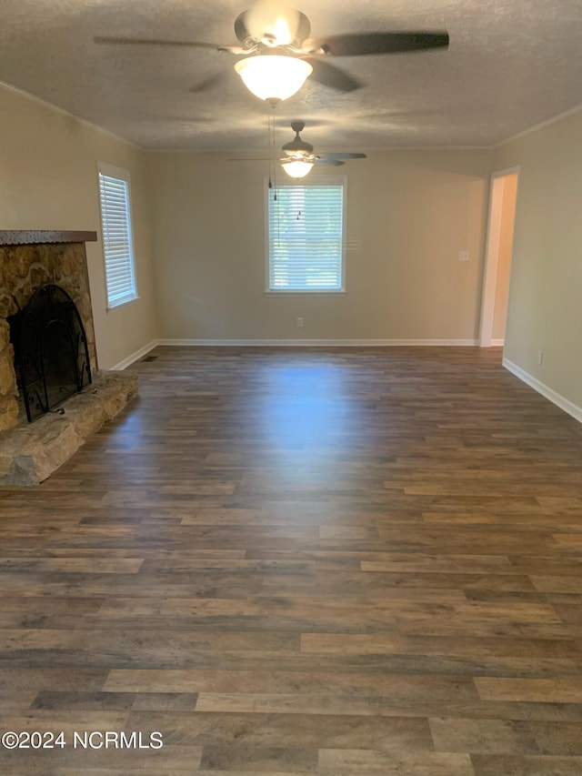 unfurnished living room featuring ceiling fan, a stone fireplace, a textured ceiling, and dark hardwood / wood-style flooring