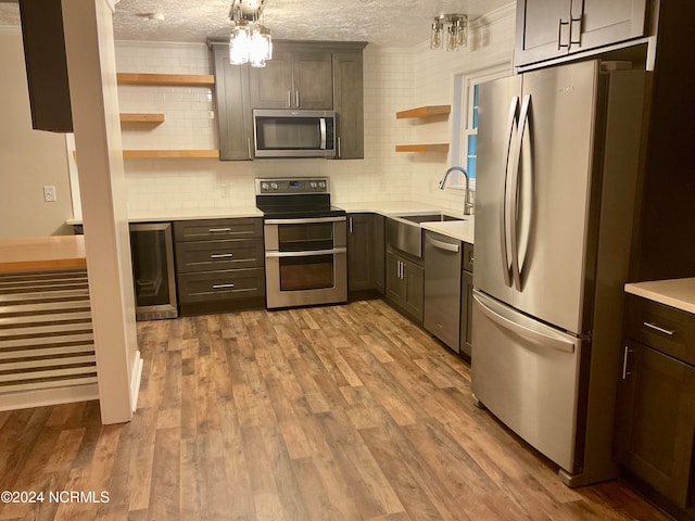 kitchen featuring appliances with stainless steel finishes, backsplash, a textured ceiling, light hardwood / wood-style flooring, and sink