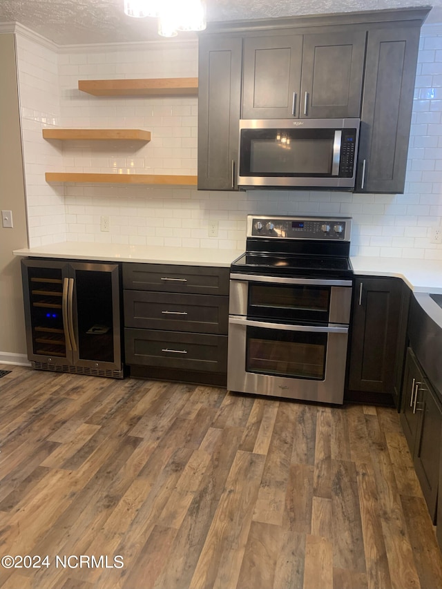 kitchen featuring beverage cooler, appliances with stainless steel finishes, hardwood / wood-style floors, and crown molding