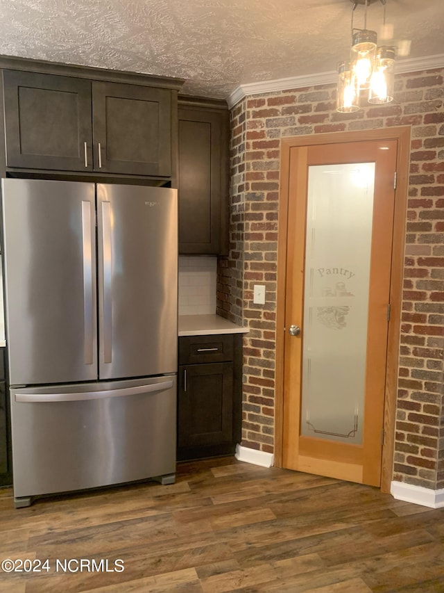 kitchen with stainless steel fridge, dark brown cabinetry, dark wood-type flooring, and brick wall