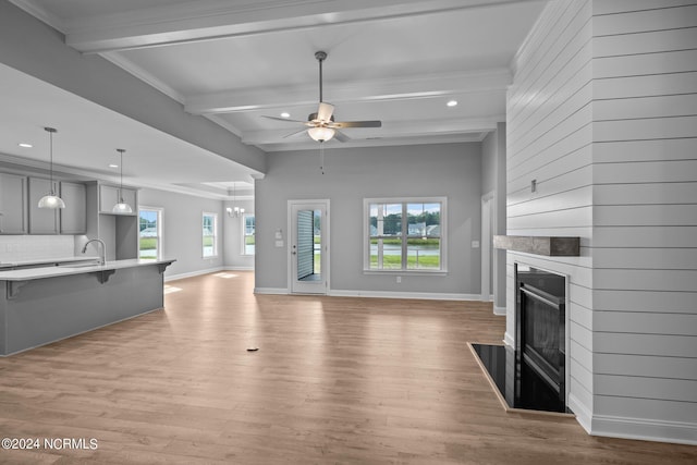 unfurnished living room with ceiling fan, light hardwood / wood-style floors, a wealth of natural light, and beamed ceiling