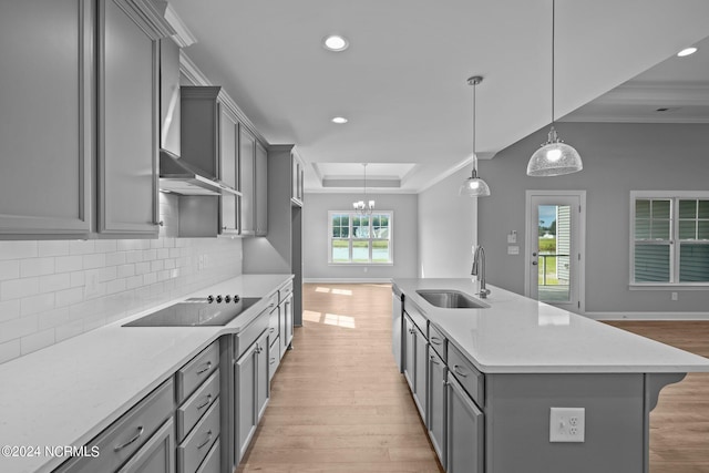 kitchen featuring black electric cooktop, a tray ceiling, a kitchen island with sink, pendant lighting, and sink