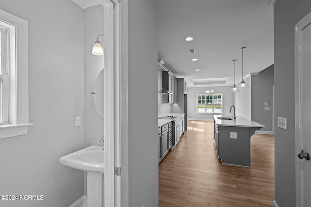 kitchen featuring a center island with sink, black electric stovetop, decorative light fixtures, dark wood-type flooring, and sink