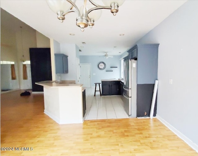 kitchen featuring ceiling fan with notable chandelier, light hardwood / wood-style floors, stainless steel fridge, kitchen peninsula, and blue cabinets