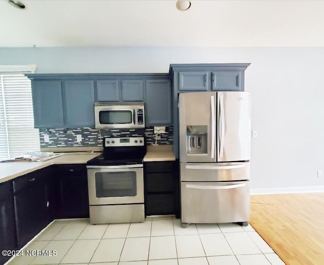 kitchen featuring light wood-type flooring, stainless steel appliances, blue cabinetry, and decorative backsplash