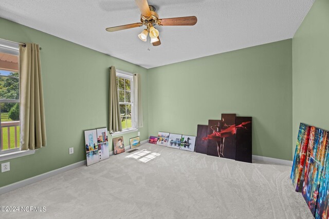 recreation room featuring a textured ceiling, a healthy amount of sunlight, light carpet, and ceiling fan