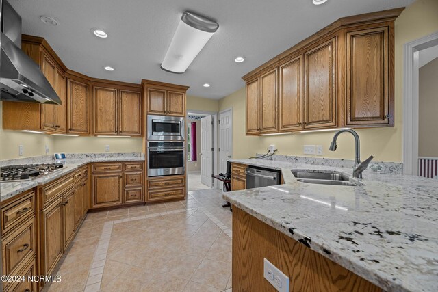 kitchen featuring wall chimney exhaust hood, light stone countertops, light tile patterned floors, stainless steel appliances, and sink