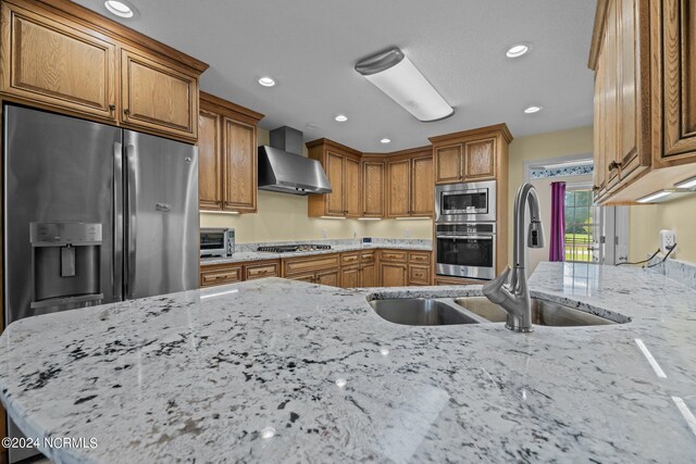 kitchen featuring wall chimney exhaust hood, appliances with stainless steel finishes, light stone countertops, and sink