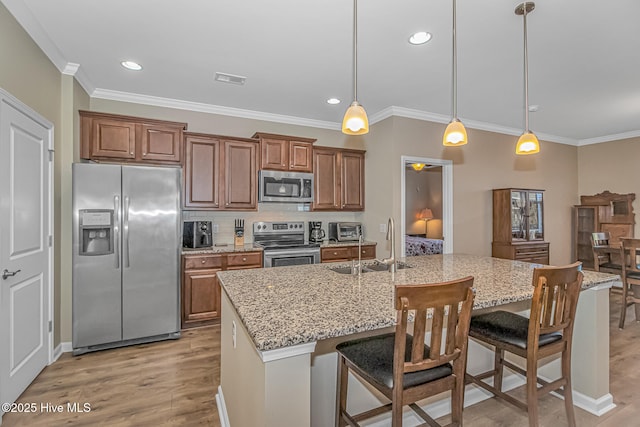 kitchen with appliances with stainless steel finishes, hanging light fixtures, an island with sink, light stone countertops, and a breakfast bar