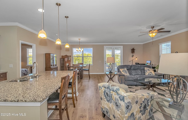 living room with sink, light wood-type flooring, crown molding, and ceiling fan with notable chandelier