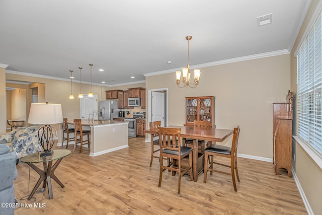 dining area featuring sink, an inviting chandelier, ornamental molding, and light hardwood / wood-style floors