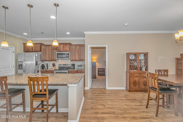 kitchen featuring stainless steel appliances, hanging light fixtures, crown molding, light stone counters, and sink