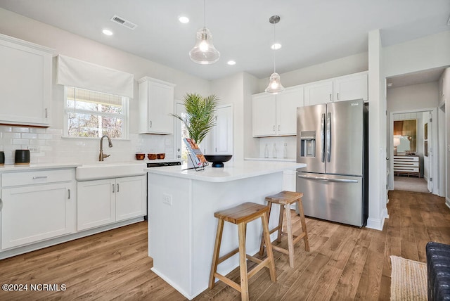 kitchen with a kitchen island, stainless steel fridge, white cabinetry, and light hardwood / wood-style floors