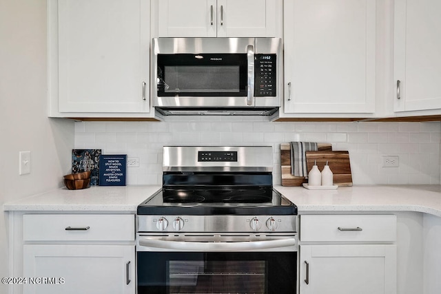 kitchen with white cabinets, appliances with stainless steel finishes, light stone countertops, and backsplash