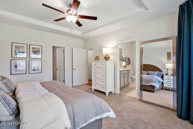 bedroom featuring a raised ceiling, ensuite bath, light carpet, and ceiling fan